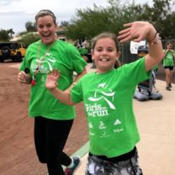 One coach and one participant wearing green shirts smiling while running in the program